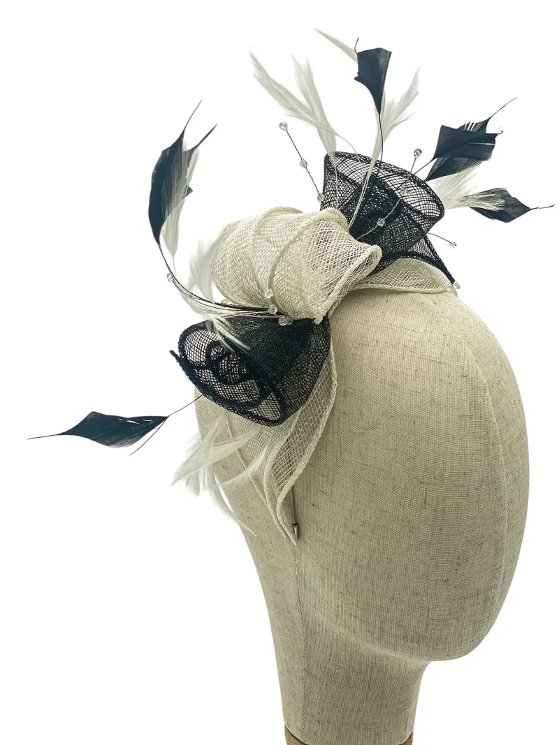 Beige fascinator hat with black mesh ribbon and white feathers displayed on a dress form