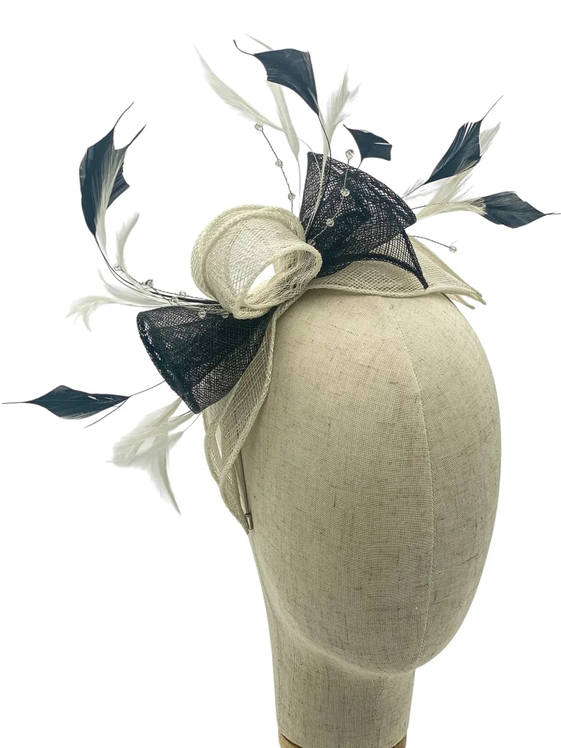 Decorative fascinator on a dress form: beige net bow with black mesh and white feathers.