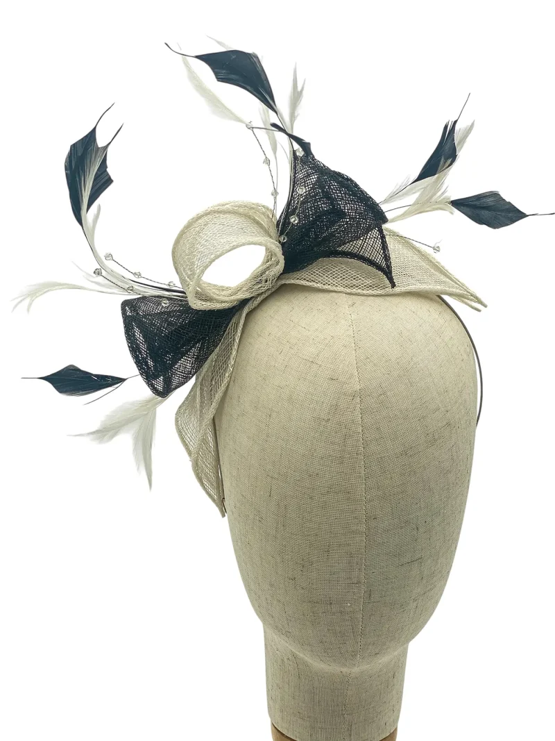 Beige fascinator hat with black mesh, pale ribbon loops, and white feathers displayed on a dress form mannequin head.