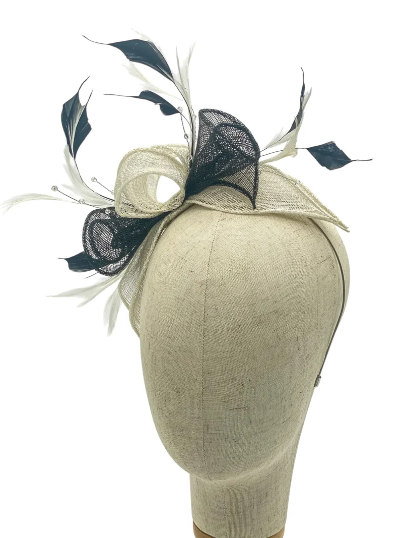 Beige mannequin head wearing a decorative fascinator with cream mesh loops, black mesh accents, and white feathers against a white background.