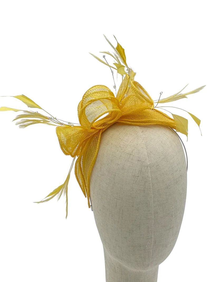 Beige dress form wearing a yellow fascinator with netted bow and feather accents.