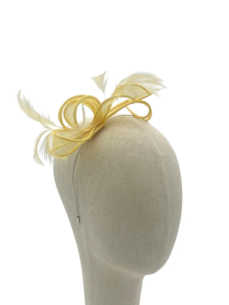 Dainty lemon minimalist sculptural fascinator with twisted loops and feather, three-quarter view on a mannequin head
