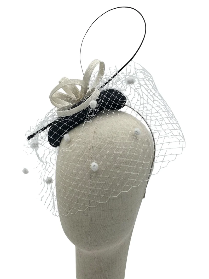 Black and white sinamay pillbox fascinator with looped sinamay and polka-dot veil, side three-quarter view on a mannequin head