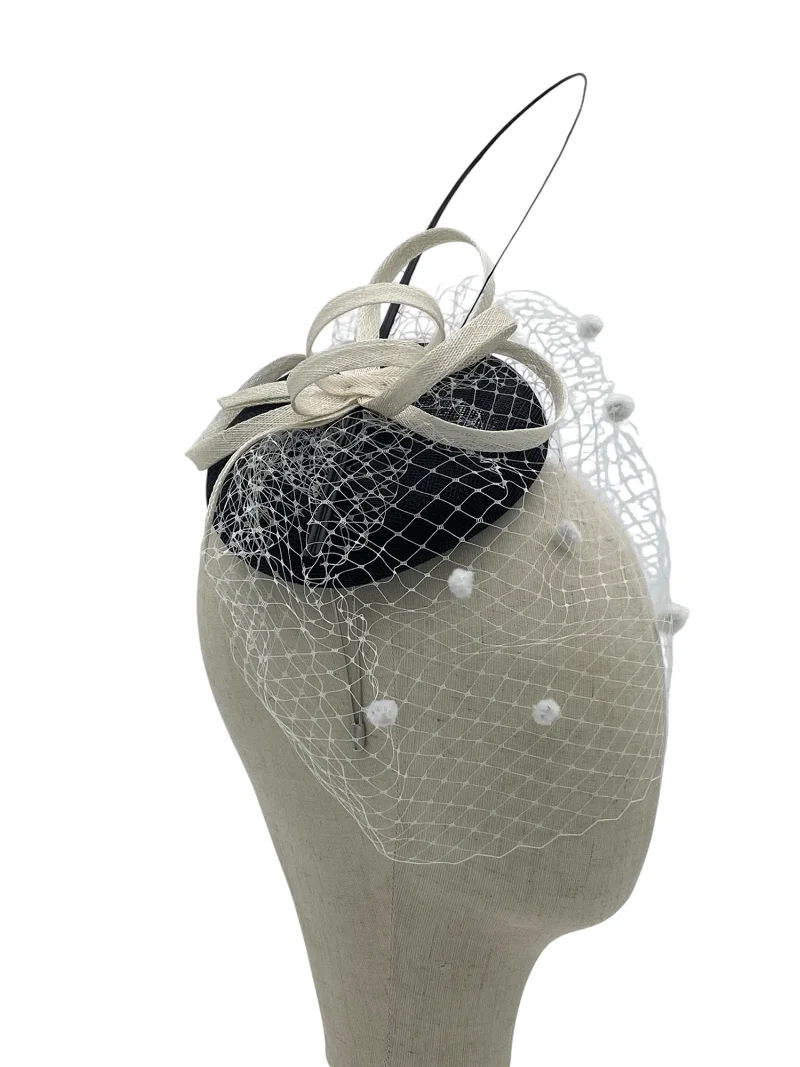 Black and white sinamay pillbox fascinator with upright quill and polka-dot birdcage veil, angled view on a mannequin head