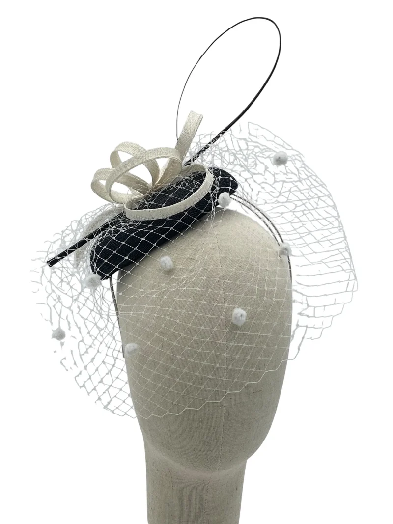 Black and white sinamay pillbox fascinator with polka-dot birdcage veil and sinamay loops, front-angle view on a mannequin head