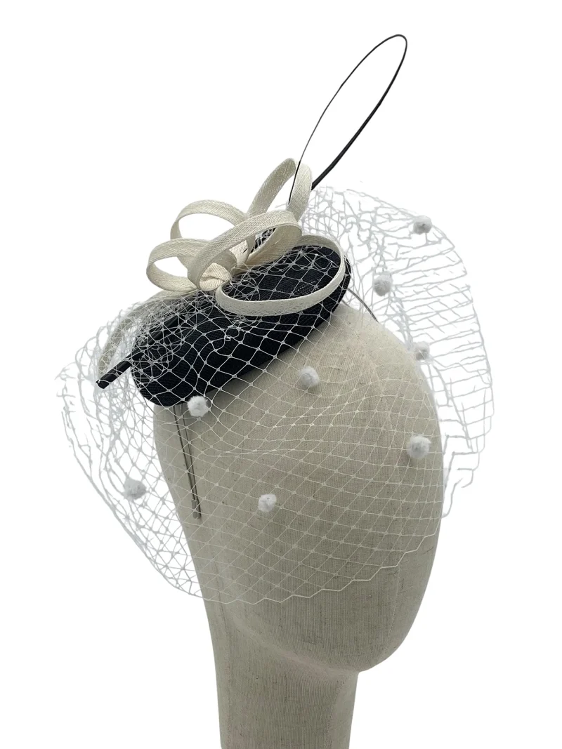 Black and white sinamay pillbox fascinator with polka-dot birdcage veil and looped trim, three-quarter view on a mannequin head