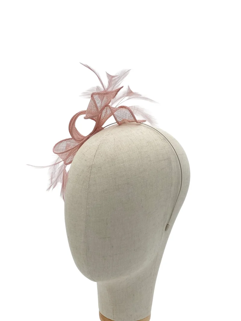 Beige mannequin head wearing a blush pink fascinator with netting and feathers on top of the head form.