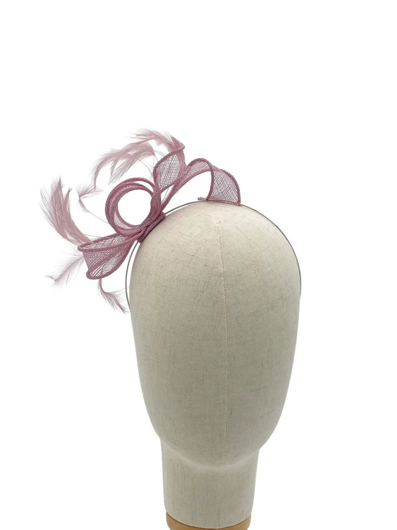 Beige mannequin head and torso wearing a pink fascinator with netting and feathers on the left side of the head area, against a white background.